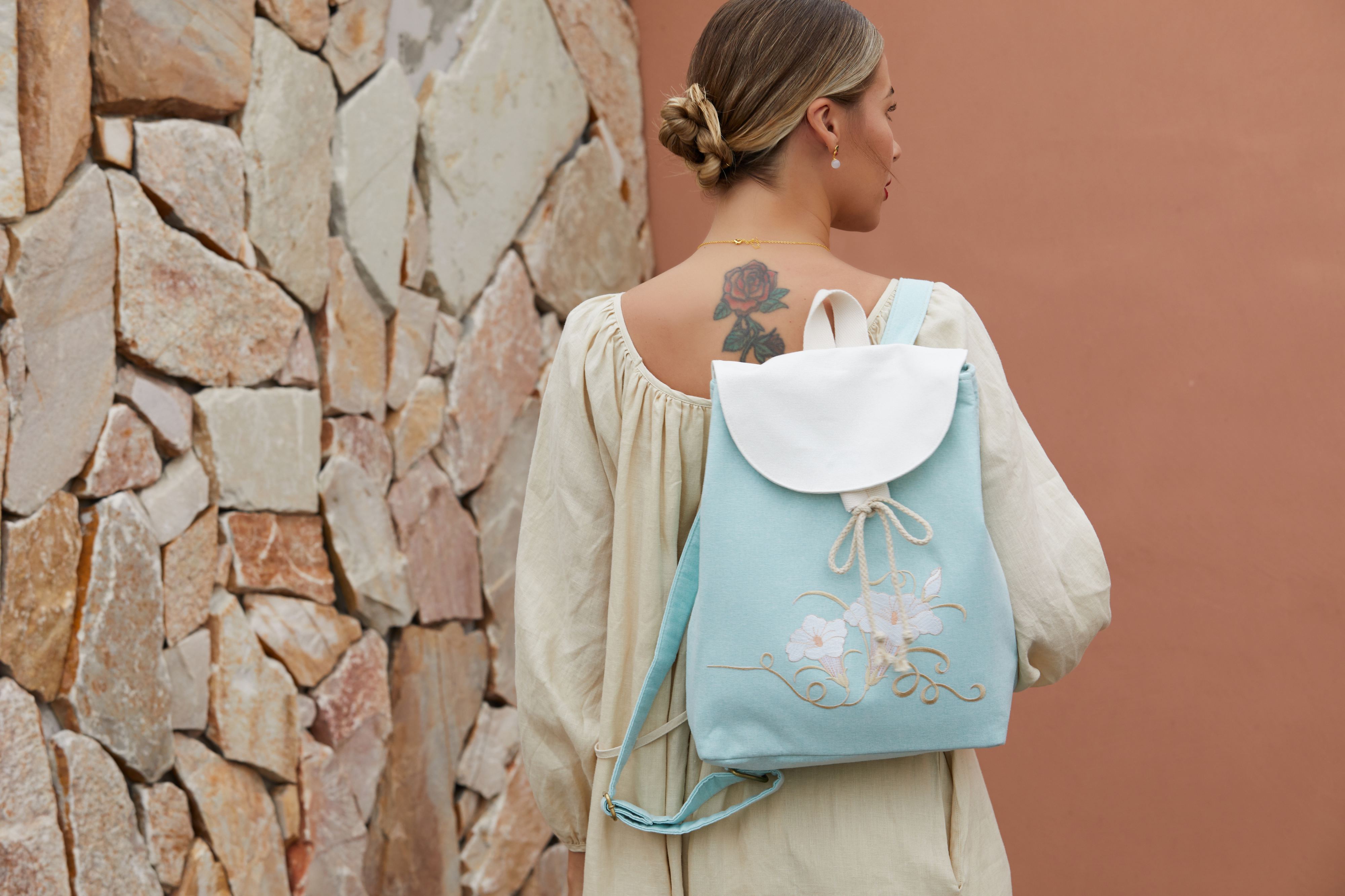 Model wearing green canvas backpack with embroidered morning glory design, blending traditional elegance with contemporary functionality.