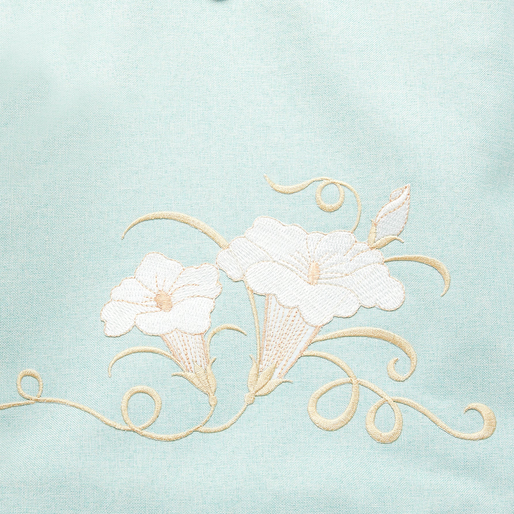 Close-up of hand-embroidered morning glory design on green canvas backpack, showcasing intricate floral stitching and vibrant colors.