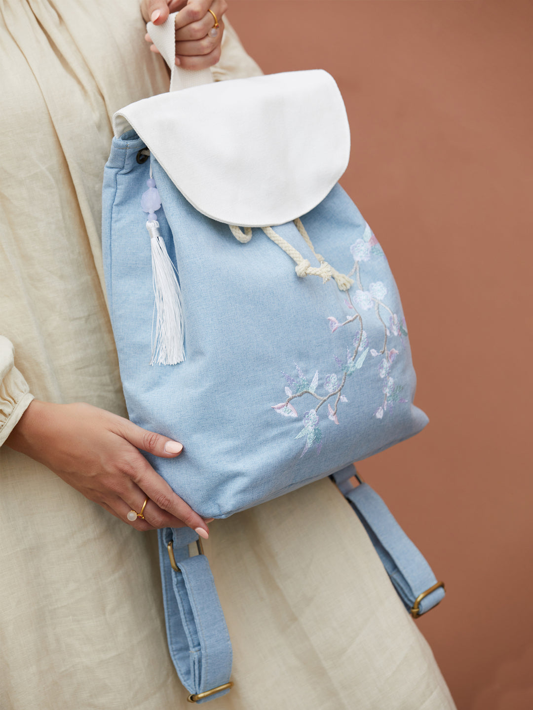 Blue canvas backpack with embroidered plum blossoms, placed on a wooden table with natural lighting, enhancing the handcrafted design.