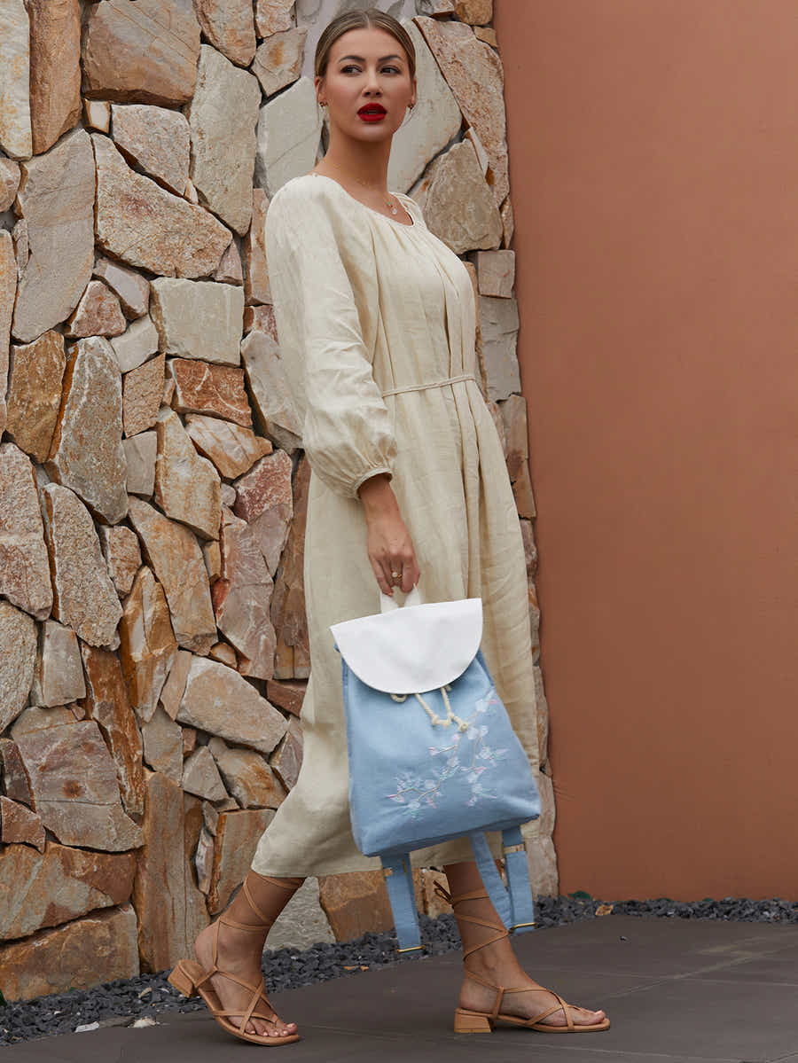 Blue canvas backpack with embroidered plum blossoms, placed on a wooden table with natural lighting, enhancing the handcrafted design.