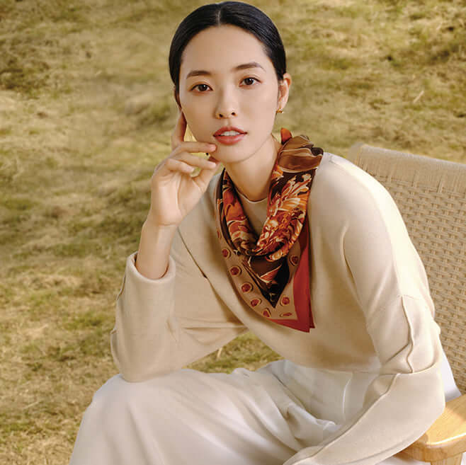 Woman wearing luxurious silk scarf with exquisite peony design, seated outdoors in a modern and elegant setting.