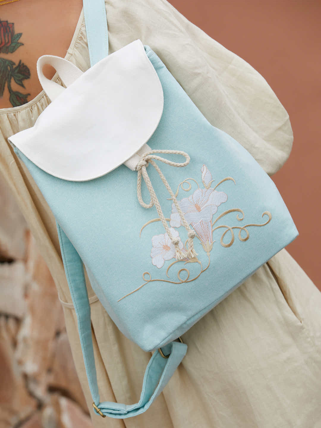 Model wearing green canvas backpack with embroidered morning glory design, blending traditional elegance with contemporary functionality.