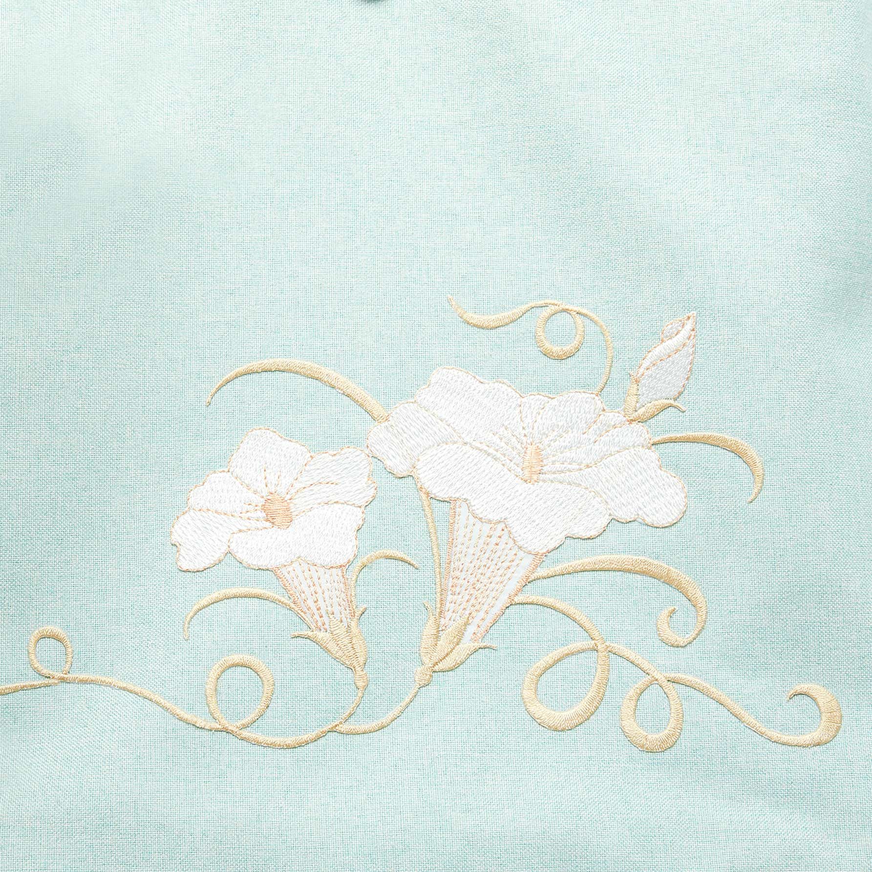 Close-up of hand-embroidered morning glory design on green canvas backpack, showcasing intricate floral stitching and vibrant colors.