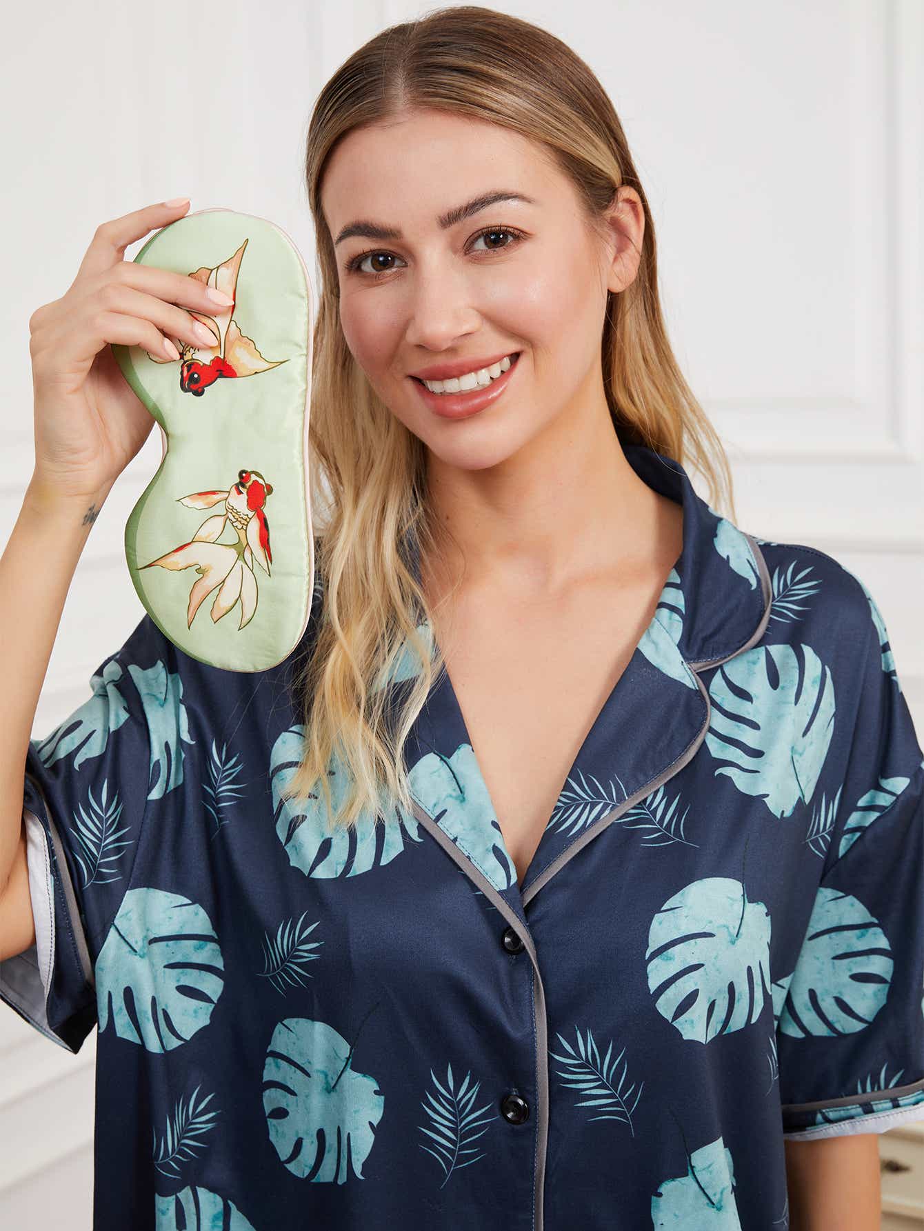 Green silk eye mask with goldfish design, placed on a soft surface to highlight its delicate craftsmanship and vibrant design.