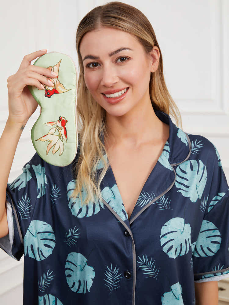 Green silk eye mask with goldfish design, placed on a soft surface to highlight its delicate craftsmanship and vibrant design.