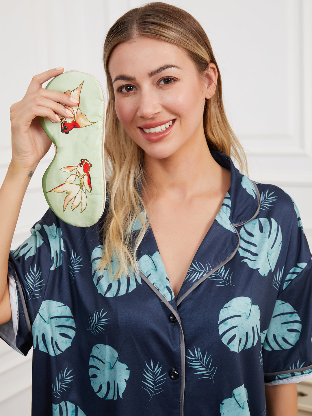 Green silk eye mask with goldfish design, placed on a soft surface to highlight its delicate craftsmanship and vibrant design.