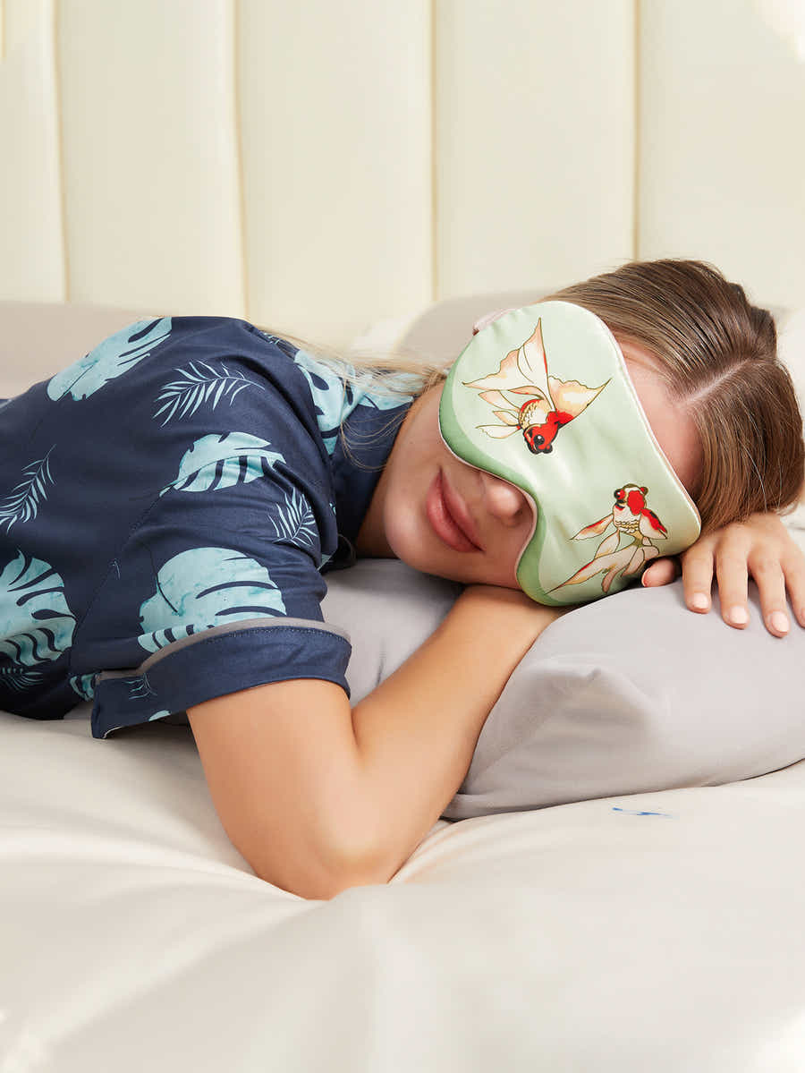 Person relaxing with green silk eye mask featuring goldfish design, perfect for meditation and peaceful rest.