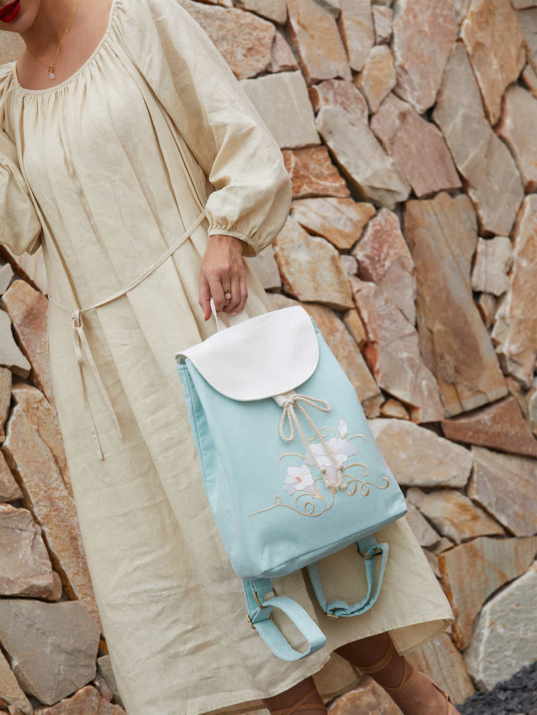 Green canvas backpack with embroidered morning glory design, placed in a tranquil garden setting, enhancing the artistic beauty of the piece.