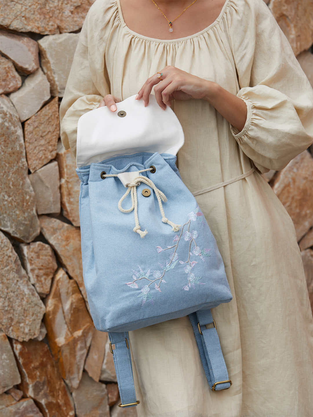 Detail of blue canvas backpack with embroidered plum blossom design, featuring high-quality zippers and brand logo.