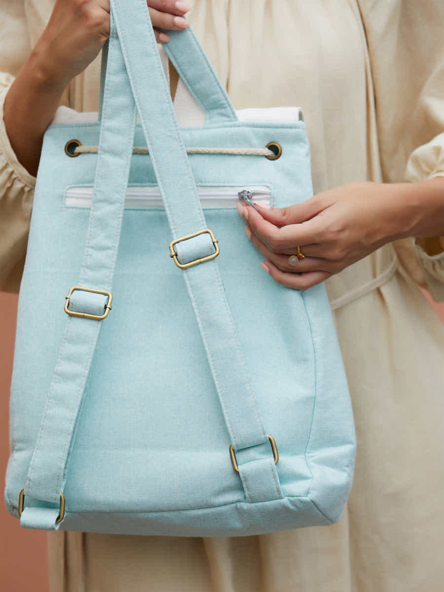 Detailed shot of green canvas backpack with embroidered pear blossoms, highlighting high-quality zippers and brand logo.