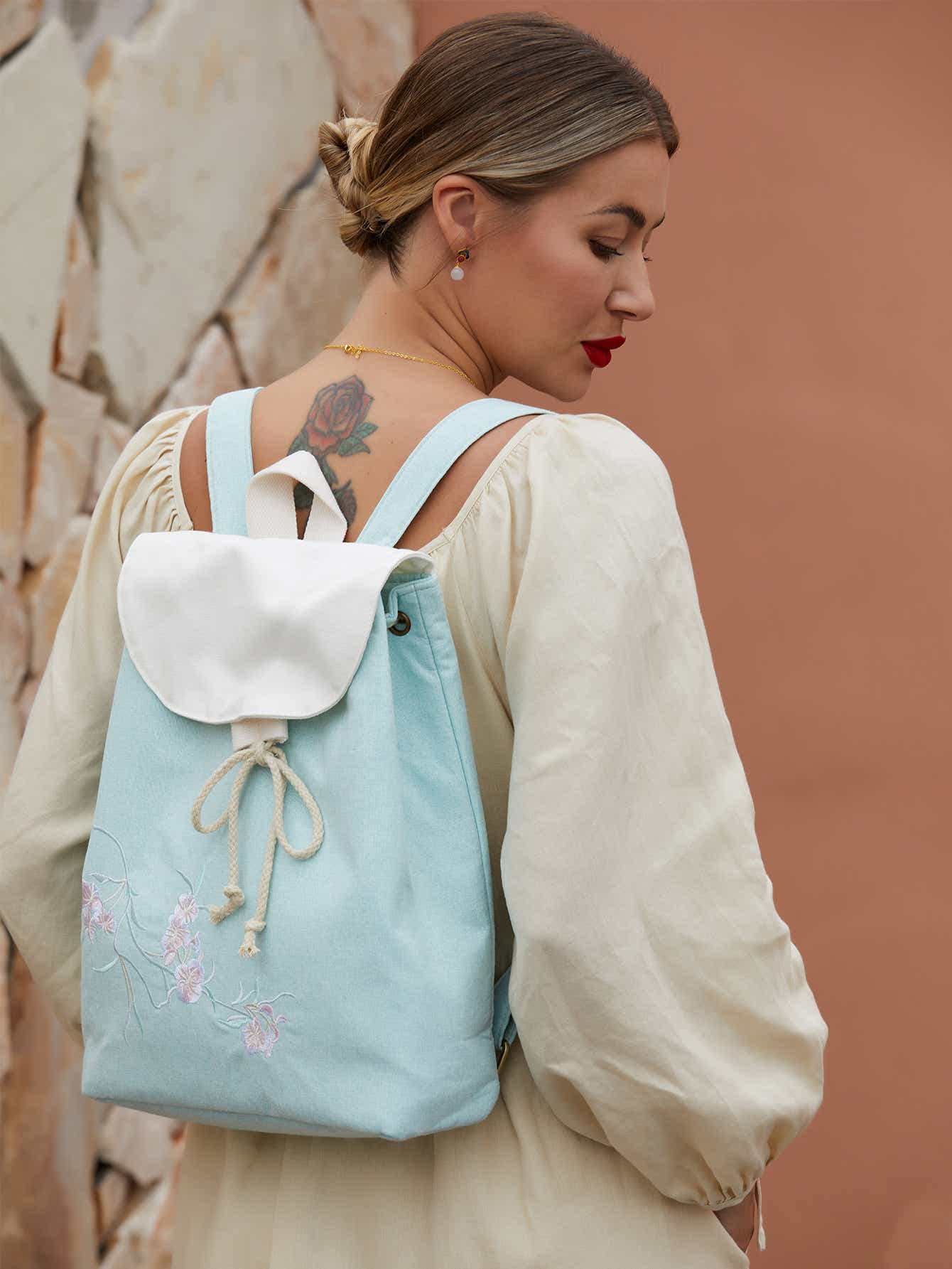 Back view of green canvas backpack with adjustable straps, featuring a beautiful embroidered pear blossom design.