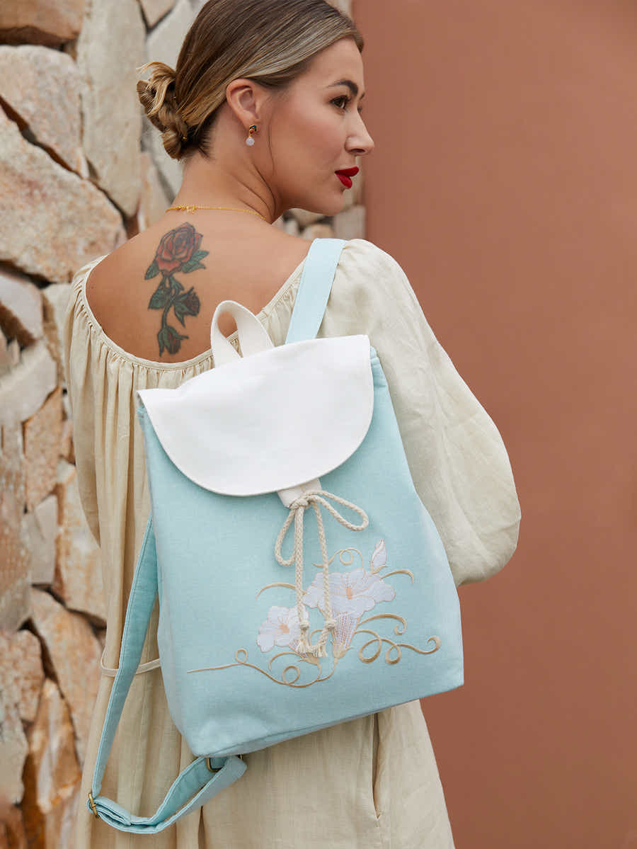 Model wearing green canvas backpack with embroidered morning glory design, blending traditional elegance with contemporary functionality.