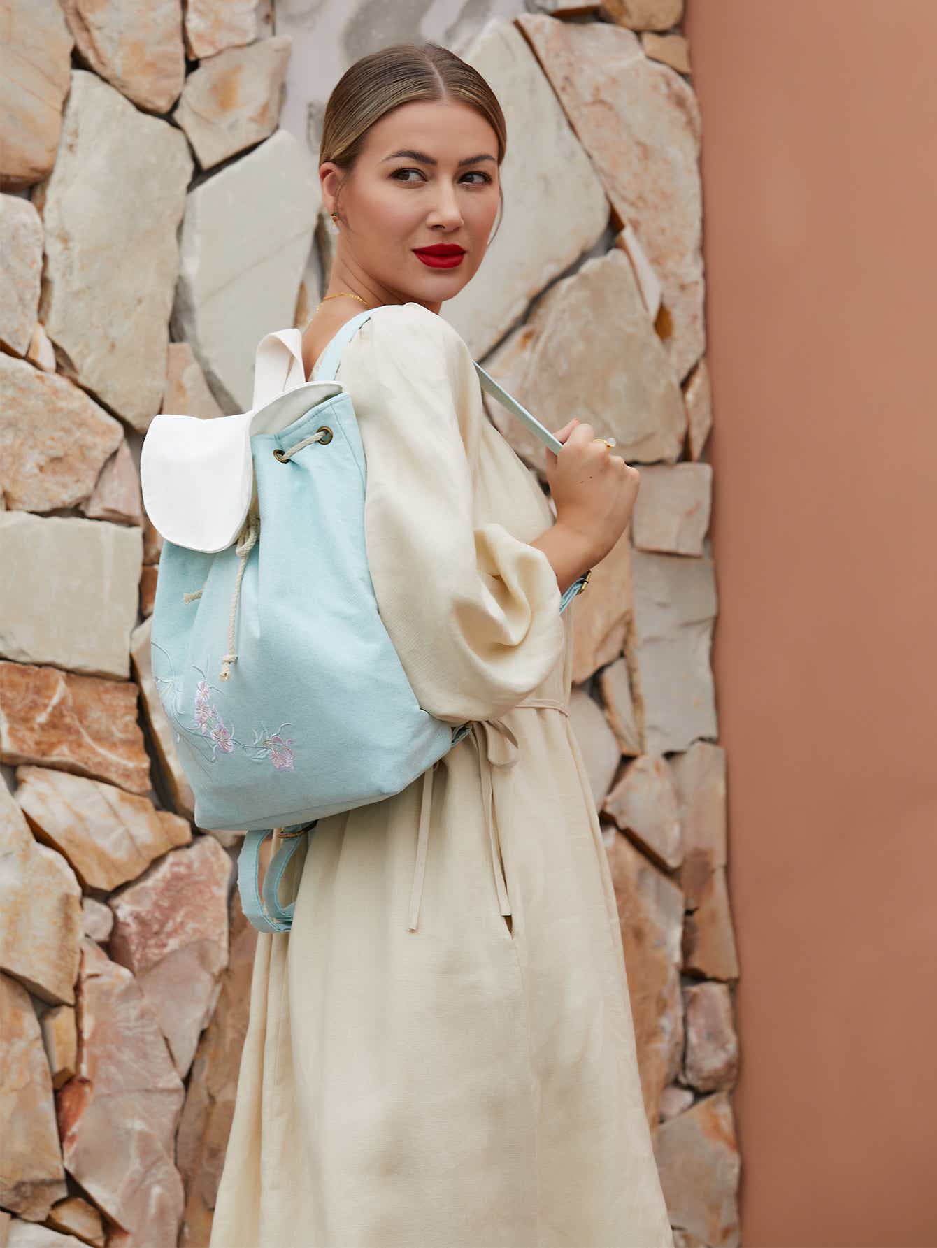 Model wearing green canvas backpack with embroidered pear blossom design, blending traditional elegance with modern practicality.