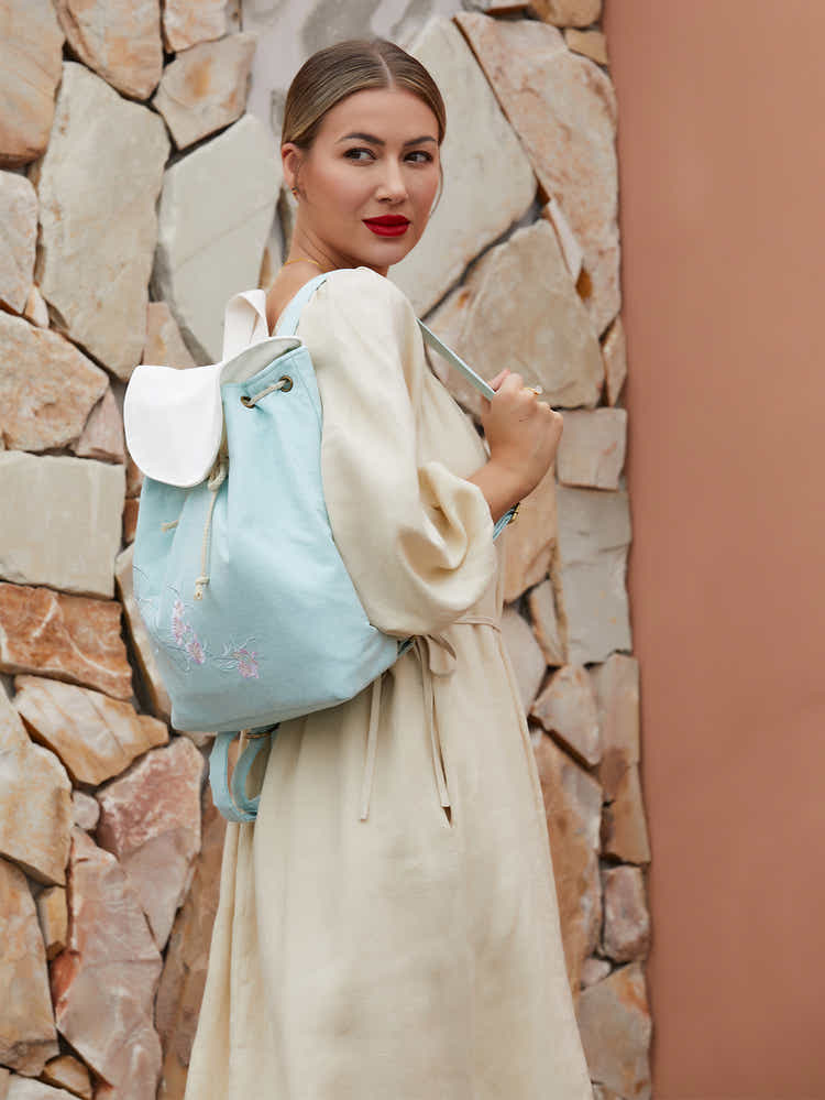 Model wearing green canvas backpack with embroidered pear blossom design, blending traditional elegance with modern practicality.