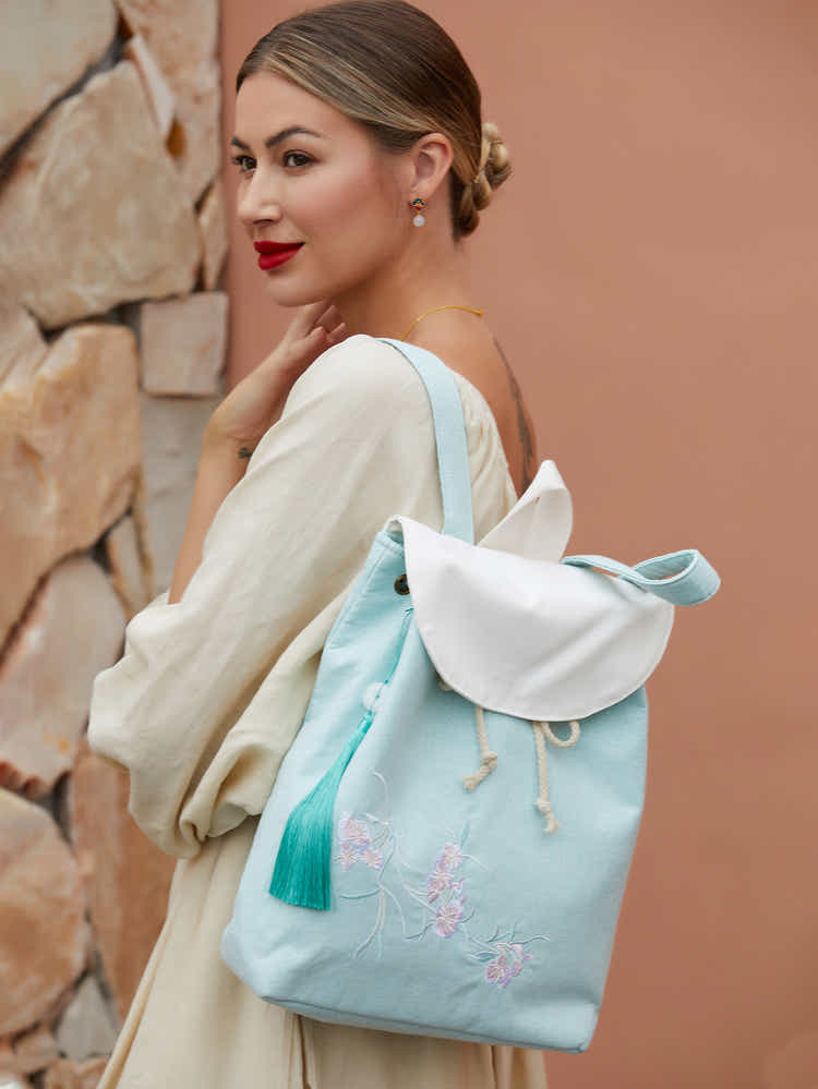 Side view of green canvas backpack with embroidered pear blossoms, highlighting the sleek silhouette and durable material.