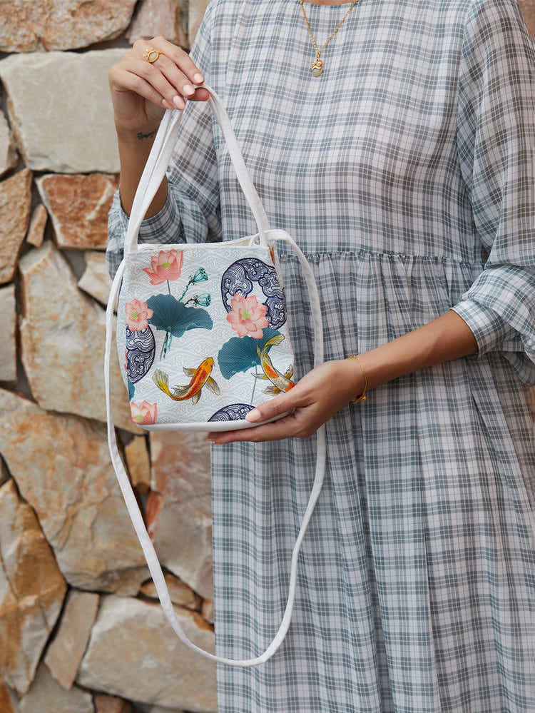 Detailed shot of white canvas crossbody bag with The Lotus Gatherers design, featuring high-quality zippers and sustainable craftsmanship.